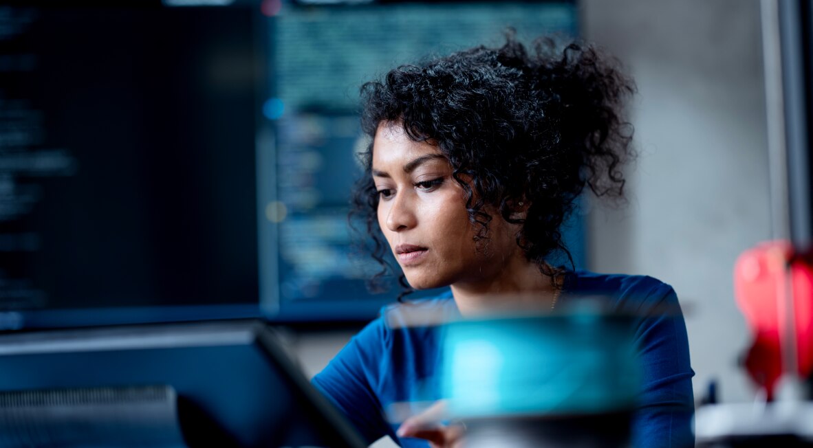 A woman focused on coding with multiple screens in the background.