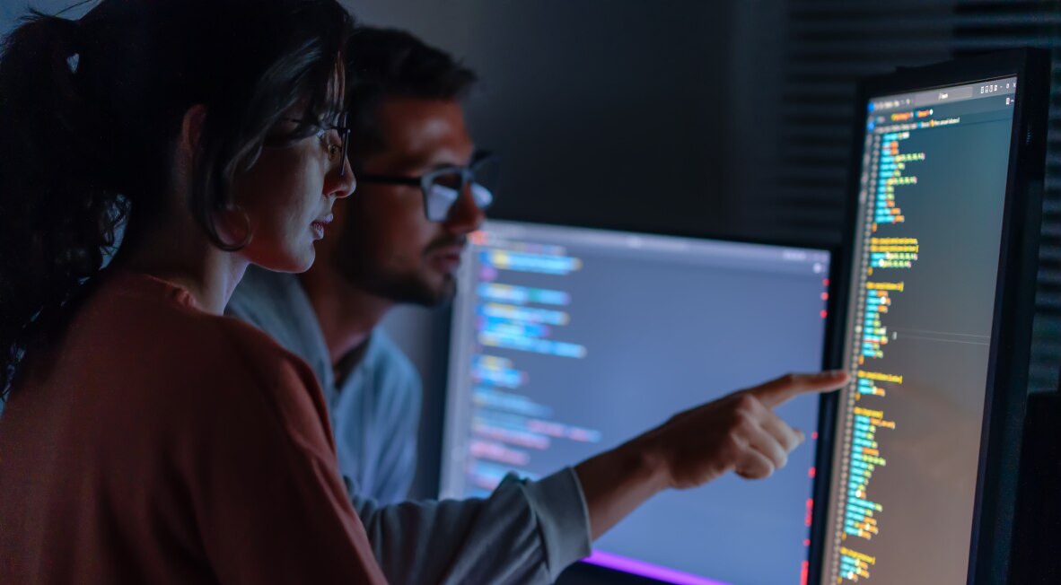 Colleagues collaborating while pointing at code on a monitor.