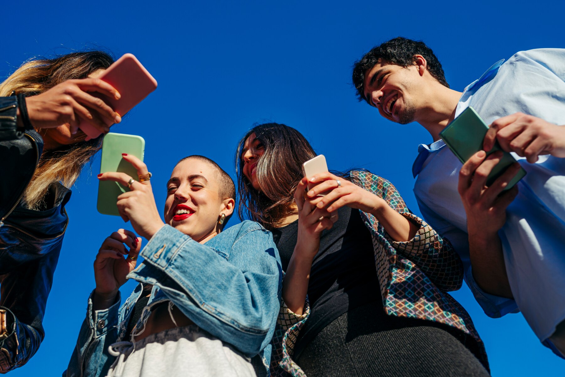 A group of people interacting with their smartphones outdoors, representing social connectivity and the widespread integration of mobile technology in daily life.