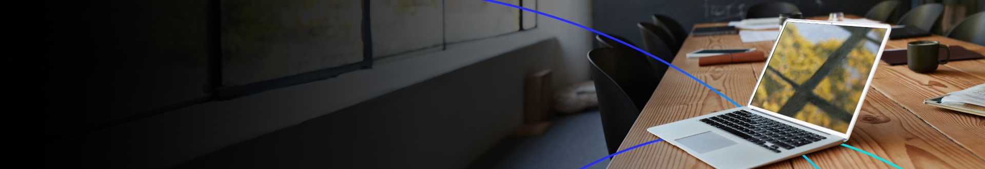 An open laptop on a conference table in a modern office setting.