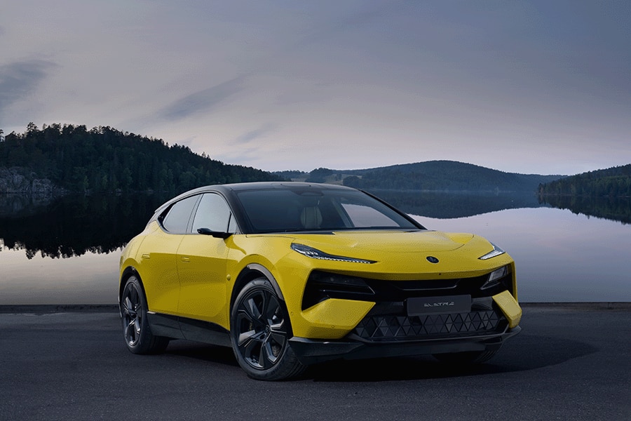 Yellow Lotus SUV parked by a serene lake with forested hills in the background.