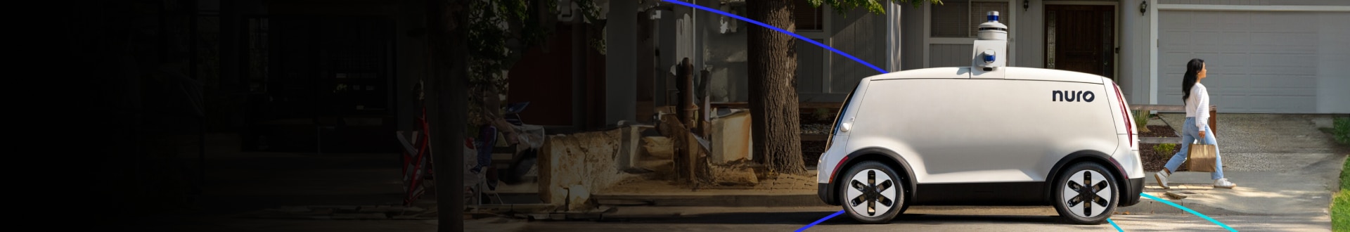 Nuro autonomous delivery vehicle parked in front of a house with a person walking nearby.