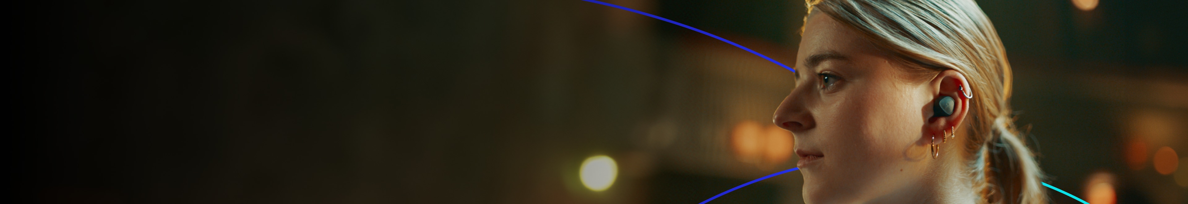 Woman wearing wireless earbud with multiple gold earrings, showcasing modern audio technology and sleek wearable design.