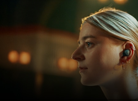 Woman wearing wireless earbud with multiple gold earrings, showcasing modern audio technology and sleek wearable design.