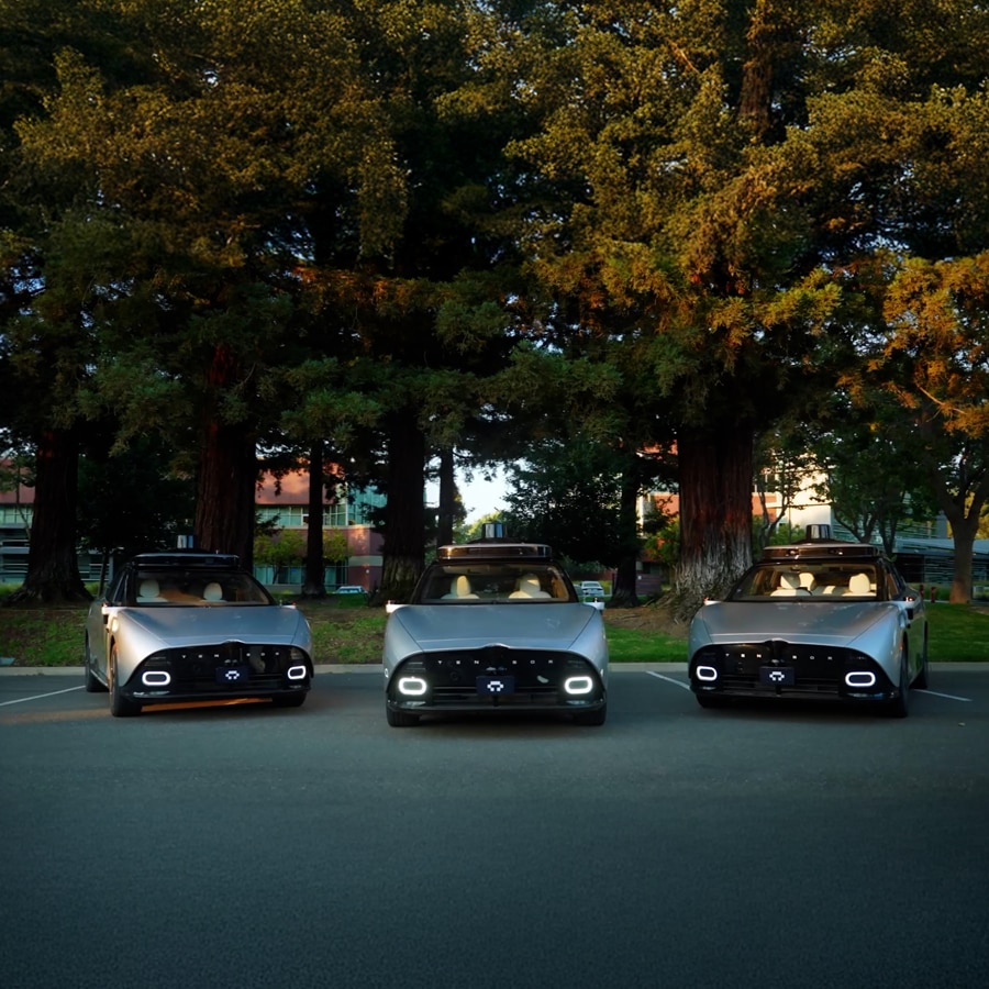 Fleet of autonomous vehicles parked beneath large trees.