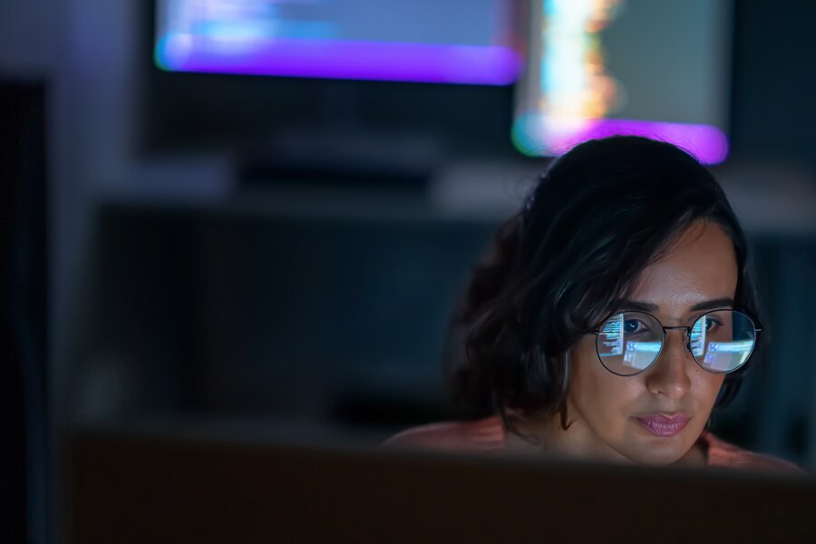 Woman with glasses reflecting code, working at a computer.