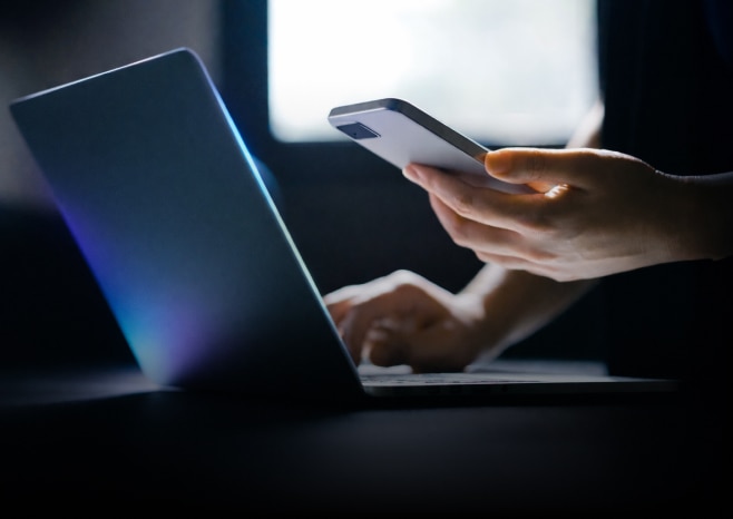 Mobile and PC - Person using a smartphone while working on a laptop.