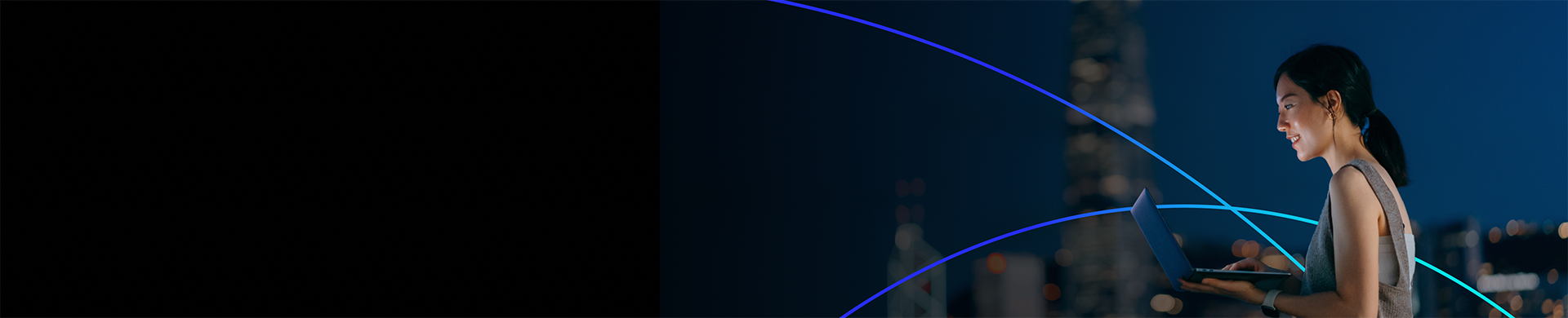 Smiling woman using a laptop outdoors at night with city lights in the background.