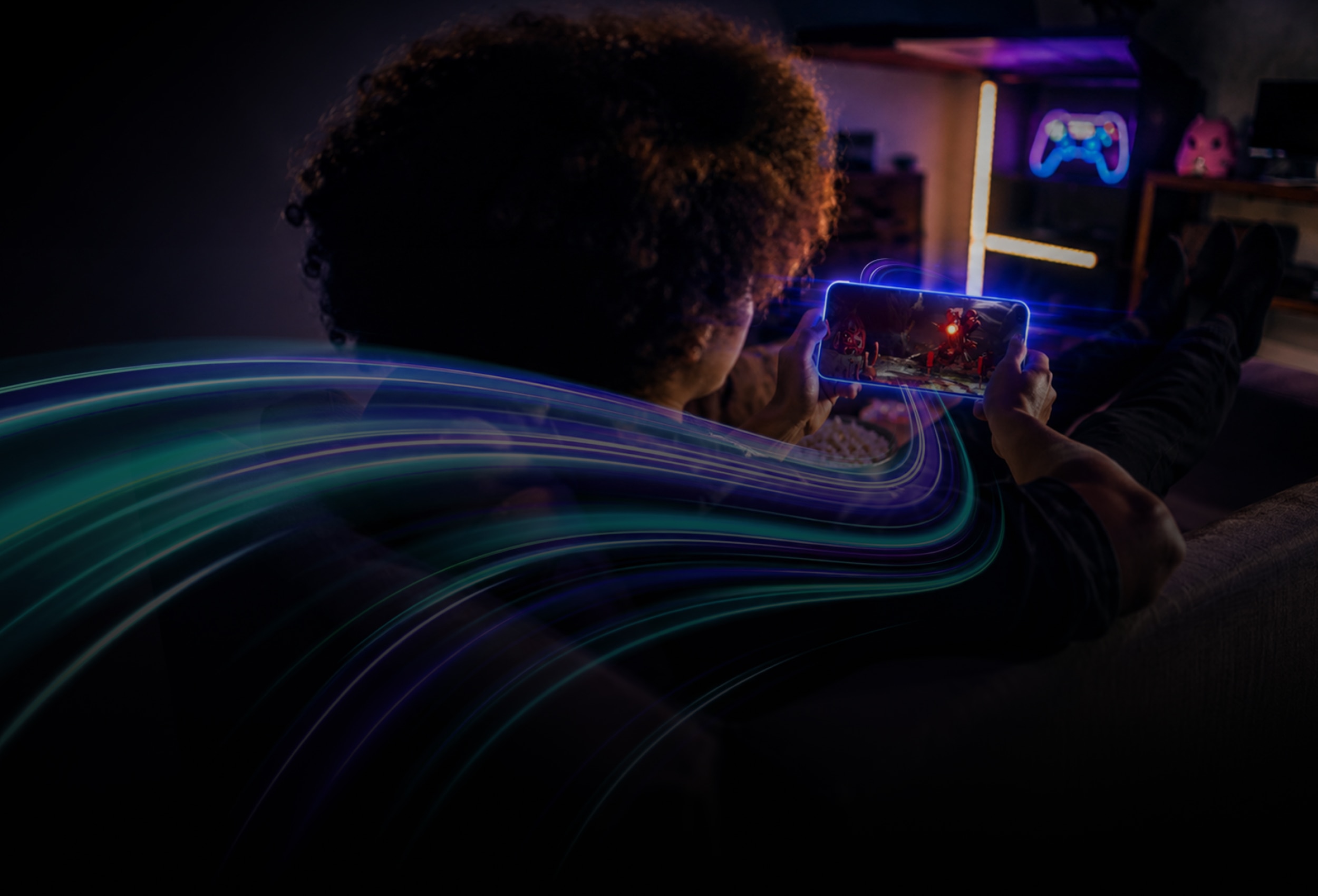 Arm CSS for Mobile 2 consumer hero: Person relaxing on a sofa while playing a mobile game on a smartphone, with colorful light trails illustrating fast, immersive mobile connectivity.