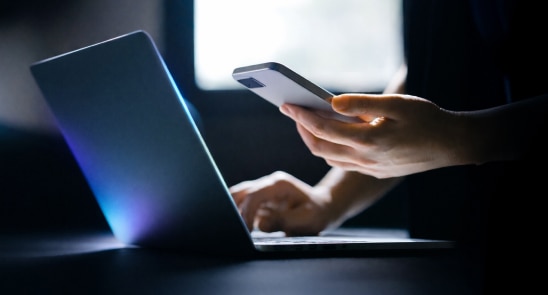 Mobile & PC -Person using a smartphone while working on a laptop.