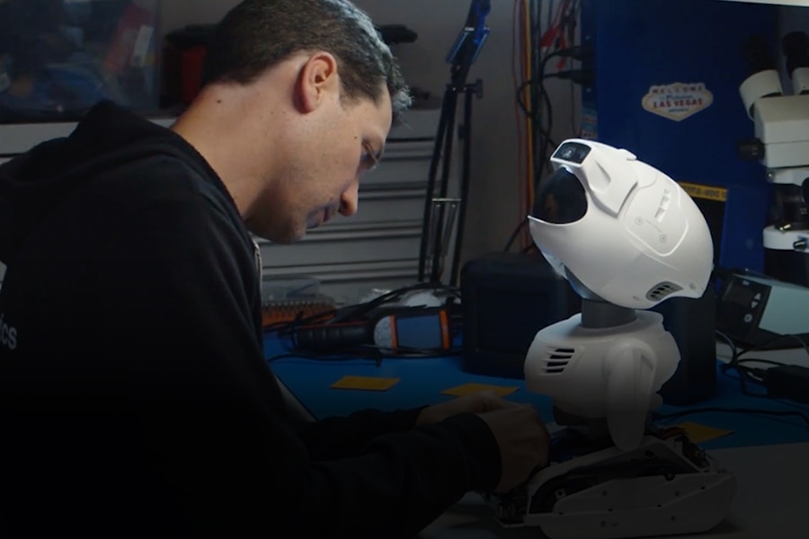 Engineer working on a small humanoid robot in a lab setting.